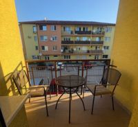 2 iz apartmán v príjemnej lokalite  - Balkón 2-izbového bytu vo Vlčkovciach so stolom a stoličkami, výhľad na bytovku.