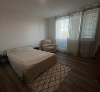2 iz apartmán v príjemnej lokalite  - Spálňa v 2-izbovom byte s posteľou, kreslom a podlahou s dreveným dekorom.
