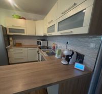 2 iz apartmán v príjemnej lokalite  - Kuchyňa v 2-izbovom byte s podlahou s dreveným dekorom a svetlým nábytkom.