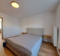 Prenájom kompletne zrekonštruovaného 2-izbového bytu s balkónom - Spálňa s posteľou a nočnými stolíkmi, podlaha s dreveným dekorom v 2-izbovom byte.