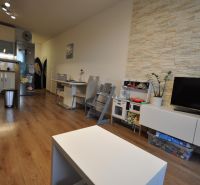3-IZBOVÝ TEHLOVÝ BYT V DUBNICI NAD VÁHOM | 68 m² | BALKÓN | VLASTNÉ KÚ - Obývacia izba s podlahou s dreveným dekorom, kuchyňou, jedálenským stolom a TV skrinkou.
