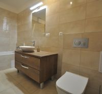 3-IZBOVÝ TEHLOVÝ BYT V DUBNICI NAD VÁHOM | 68 m² | BALKÓN | VLASTNÉ KÚ - Kúpeľňa s vaňou, umývadlom na drevenom dekore a béžovými obkladmi v 3-izbovom byte.