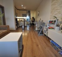 3-IZBOVÝ TEHLOVÝ BYT V DUBNICI NAD VÁHOM | 68 m² | BALKÓN | VLASTNÉ KÚ - Obývacia izba v 3-izbovom byte s podlahou s dreveným dekorom, sedacou súpravou a kuchyňou.