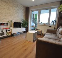 3-IZBOVÝ TEHLOVÝ BYT V DUBNICI NAD VÁHOM | 68 m² | BALKÓN | VLASTNÉ KÚ - Obývačka v 3-izbovom byte s podlahou s dreveným dekorom a kamenným obkladom na stene.