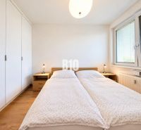 PRENÁJOM | Moderný 2-izbový byt so šatníkom v projekte Malé Krasňany – - Svetlá spálňa s veľkou posteľou, skriňou a podlahou s dreveným dekorom v 2-izbovom byte.