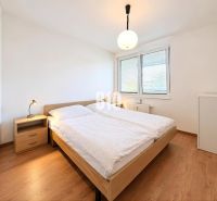 PRENÁJOM | Moderný 2-izbový byt so šatníkom v projekte Malé Krasňany – - Spálňa v 2-izbovom byte s posteľou, nočným stolíkom a podlahou s dreveným dekorom.