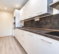 Na predaj kompletne zrekonštruovaný 3-izbový byt s lodžiou – Košice - Kuchyňa v 3-izbovom byte s bielym nábytkom a podlahou s dreveným dekorom.