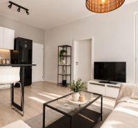 Moderný 2-izbový apartmán, balkón, sklad, Šancová-novostavba PREMIÈRE - Svetlá obývačka v 2-izbovom byte s podlahou s dreveným dekorom, bielymi skrinkami a pohovkou.