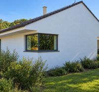 MODERNÝ 6-IZBOVÝ BUNGALOV S TERASOU A POZEMKOM 884 m² – RATNOVCE - Rodinný dom v Ratnovciach obklopený zeleňou, s veľkými oknami a jednoduchou bielou fasádou.