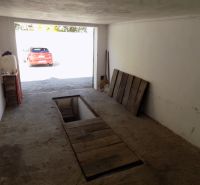 Nadštandardne vybavená garáž s pivnicou a studňou v Štúrove - Garáž so servisnou jamou, starší betónový povrch a zaparkované auto vonku.