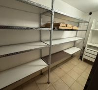NÍZKOENERGETICKÝ RODINNÝ DOM VO VALČI  – TICHÉ PROSTREDIE - Úložný priestor v rodinnom dome s kovovými regálmi a dlažbou na podlahe.