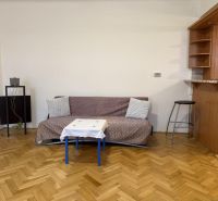 Praktický byt v širšom centre neďaleko Trnavského Mýta. Mestská ul.  - Obývacia miestnosť v 2-izbovom byte s podlahou s dreveným dekorom a kuchynským pultom.