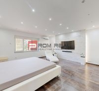 6i DVOJGENERAČNÝ DOM PO REKONŠTRUKCII S VEĽKÝM POZEMKOM A SMARTHOME –  - Svetlá spálňa v rodinnom dome s televízorom, kreslom a podlahou s dreveným dekorom.