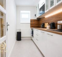 **Hotový priestor. Povolené ubytovanie. Pripravené zarábať**Airbnb** - Úzka kuchyňa s bielymi skrinkami, drevený dekor pultu, zabudovaná mikrovlnka.