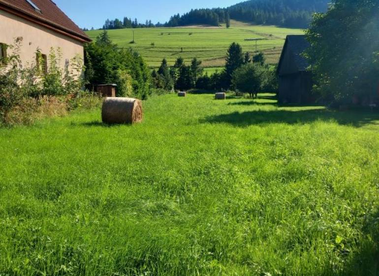 ZNÍŽENÁ CENA!!! Stavebný pozemok 1621 m2 v obci Reľov - Hagy. - Slnečná lúka s balíkmi sena pri dome, na pozadí sú svieže zelené kopce.