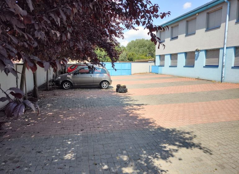 Prenájom - skladové priestory/kancelária, Vlčie hrdlo, Bratislava - Parkovisko pred modrou budovou, autá zaparkované na dlažbe, okolité stromy poskytujú tieň, kancelárie.