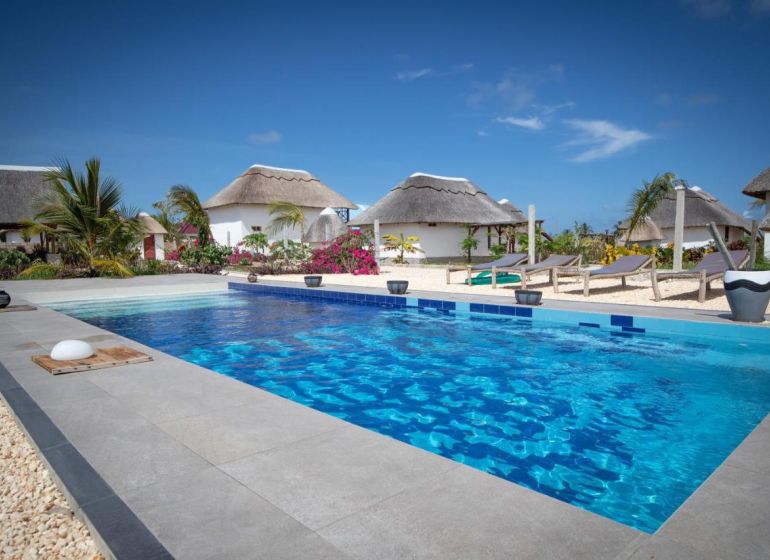 ZARIA GARDEN BUNGALOWS - Na obrázku vidno bazén, palmy a rekreačné domy s doškovými strechami v tropickom prostredí. Výstavba domov je vhodná pre relaxáciu.