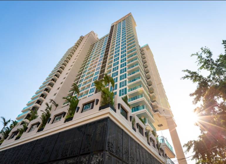 CITY GARDEN TOWER PATTAYA - Výstavba bytov v Pattayi s vysokým mrakodrapom obklopeným palmami a modrou oblohou.