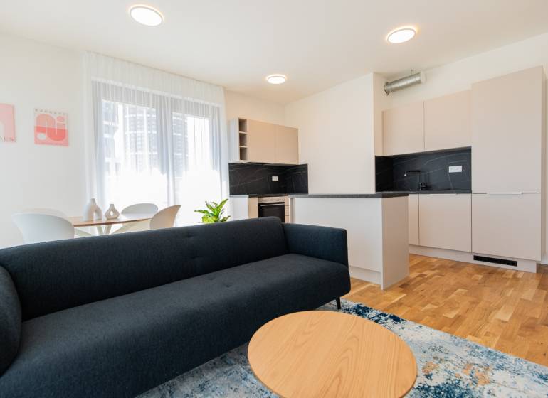 Skvelý slnečný 3i byt s balkónom v projekte METROPOLIS - Obývačka a kuchyňa v 3-izbovom byte s pohovkou, stolíkom a jedálenským stolom.