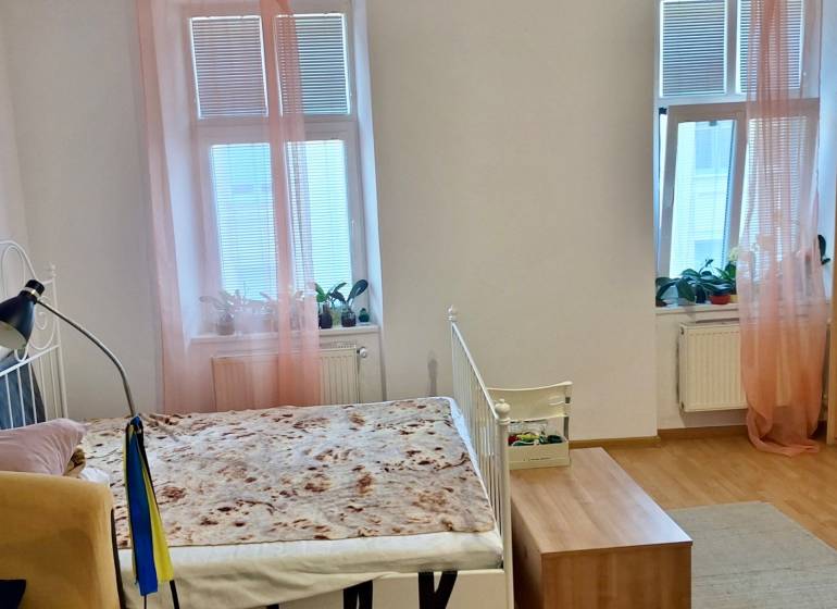 Predaj 1 izbový byt, Karpatská ulica, Bratislava I. Staré Mesto - Interiér 1-izbového bytu s posteľou, drevenou podlahou a oknami s ružovými závesmi.
