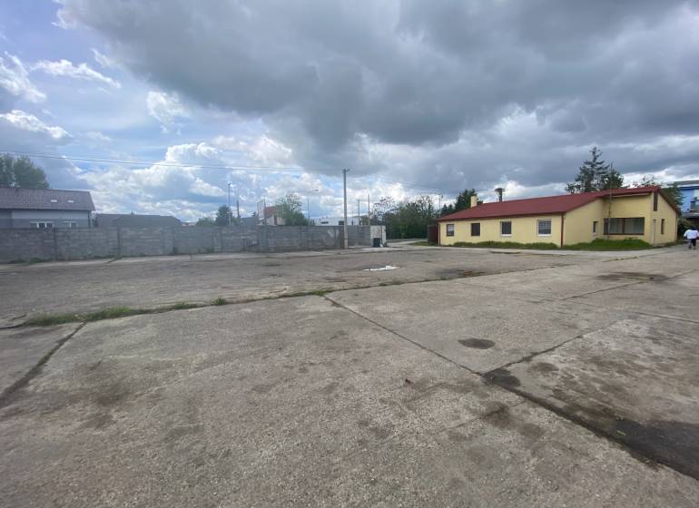Predaj/prenájom -  areál na  ul. Dvojkrížna, BA - Podunajské Biskupice - Na ulici Dvojkrížna, betónová plocha pri výrobnej budove pod zamračenou oblohou.