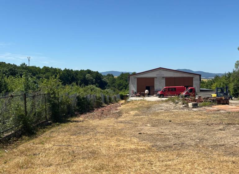 Na prenájom hala s pozemkom 4500 m² – Mníchova Lehota  - Hala so zaparkovaným autom v Mníchovej Lehote, obklopená zeleňou a oplotením.