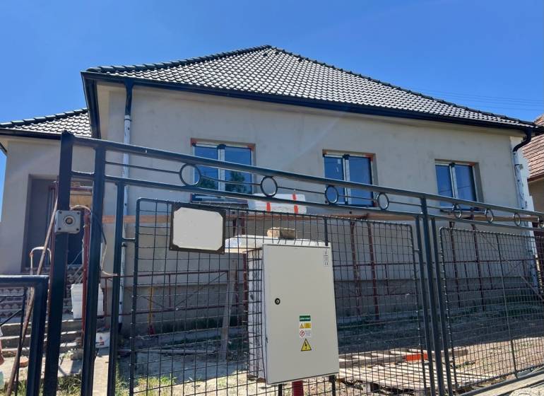 4iz RD Sasinkovo - Rodinný dom v Sasinkove na ulici Sasinkovo s nedokončenou fasádou za kovovým plotom.