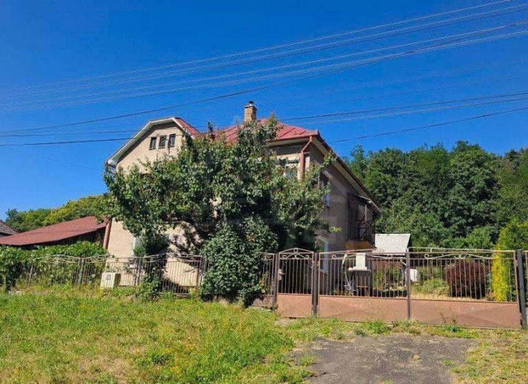 Priestranný poschodový rodinný dom v Lovinobani - Rodinný dom v Lovinobani so záhradou, bránou a zeleňou na svahu.