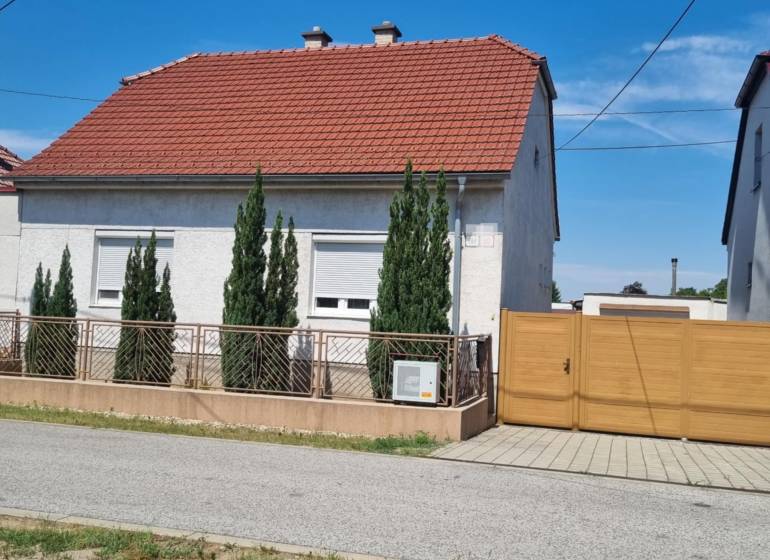 Rodinný dom na predaj - Malacky. - Rodinný dom na Riadku v Malackách s červenou strechou, predzáhradkou a drevenou bránou.