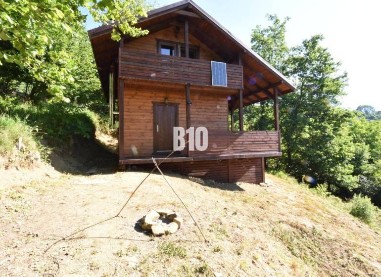 Predaj chaty a chalupy, Bytča - Drevená chata v prírode pri Bytči, obklopená stromami a ohniskom.