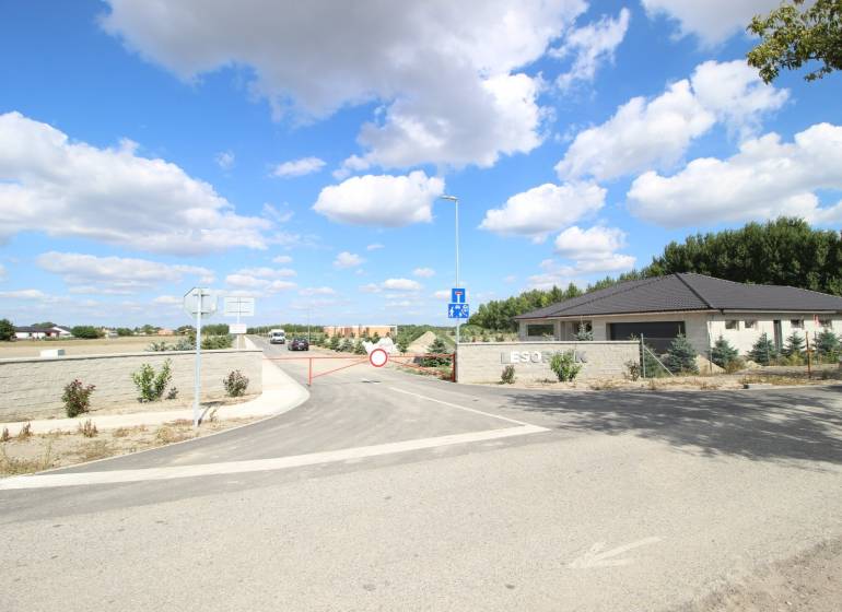 Luxusná veľkometrážna parcela za skvelú cenu Kvetoslavov,2480m2 - Brána na ulici vedie k pozemkom pre bývanie, na pozadí lesopark.