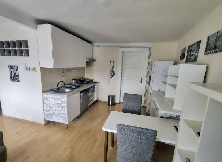 Prenájom pekný 2 izbový, Špitálska ulica, Bratislava I. Staré Mesto - Kuchyňa v 2-izbovom byte s jedálenským stolom, bielymi skrinkami a drevenou podlahou.