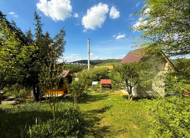 Na predaj záhrada, Trenčín-Chrasť - Záhrady v Trenčíne s výhľadom na komín, oblohu a zeleňou všade navôkol.