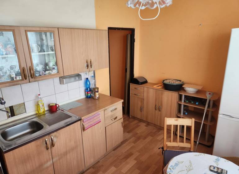 REZERVOVANÝ- 1-izbový byt, Košice, Ružová ulica - Kuchyňa v 1-izbovom byte s drevenými skrinkami, stolom a chladničkou.