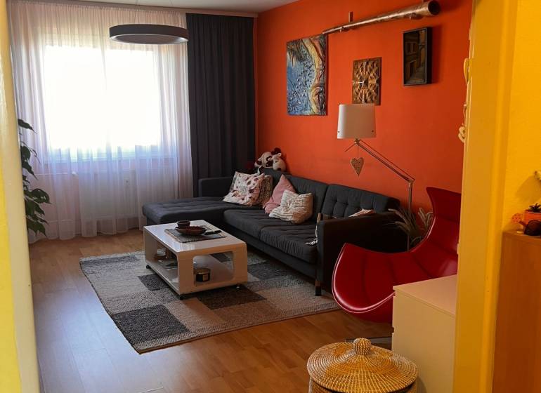 Predaj 3 izbový - Pezinok - Obývacia izba 3-izbového bytu s oranžovou stenou, sedačkou a konferenčným stolíkom.