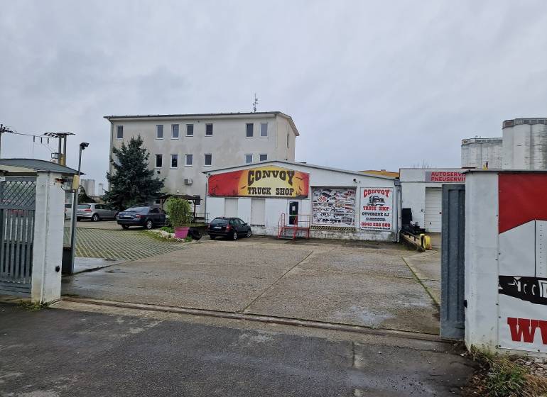 PRENÁJOM: HALA,OBCHODNÝ PRIESTOR 408 m2 v uzatvorenom areáli  - Budova Convoy Truck Shop na ulici Šamorínska, obklopená zaparkovanými autami pri sklade a halách.