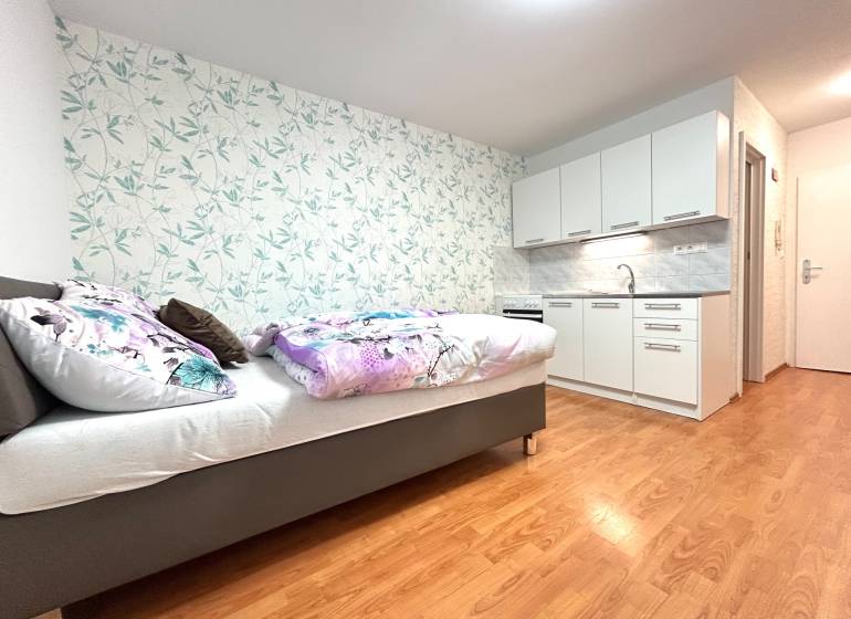 PREDAJ-GARSÓNKA-20m2-GUOTHOVA- KRAMÁRE - Garsónka s posteľou, kuchynskou linkou a kvetinovou tapetou na stene.