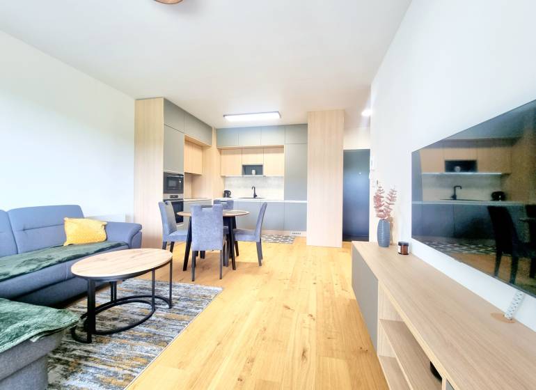 | EXKLUZÍVNE! | Krásny NOVÝ 2-izbový byt | 48m² | Čerešne - Obývacia izba v 2-izbovom byte s kuchyňou, jedálenským stolom a pohovkou.