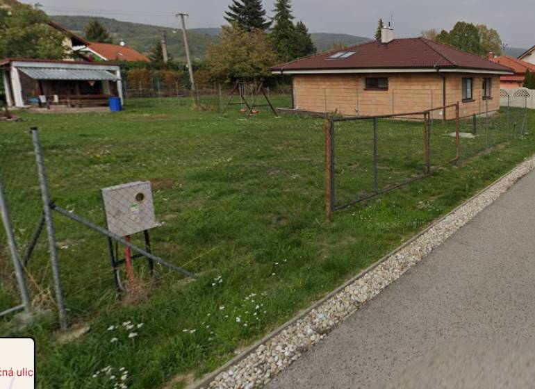 PREDAJ SP V ČASTEJ - 691 m2  ,,, ZNÍŽENÁ CENA,,, - Na ulici Slnečná pozemky: Trávnik, dom, oplotenie, budovy a stromy v pozadí.