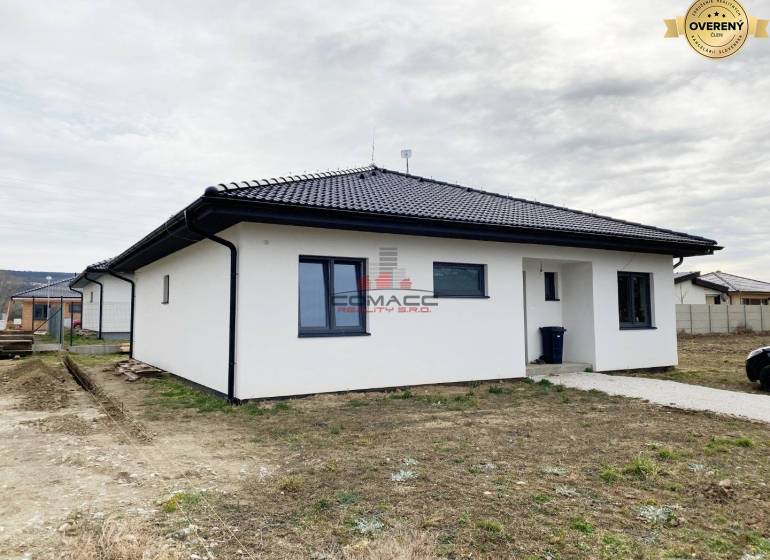 Výstavba inteligentného 4 izbového bungalovu v NM a okolí - Rodinný dom na ulici v Novom Meste nad Váhom s bielou fasádou a tmavou strechou.