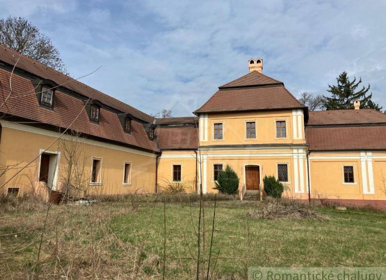 Rekonštruovaný barokový kaštieľ s kaplnkou a rozsiahlym parkom v Trávn - Historická žltá budova v Trávnici so šikmou strechou, obklopená záhradou. Zvláštne nehnuteľnosti.