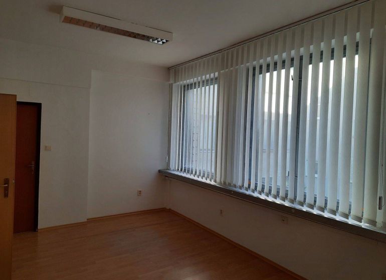 Prenájom kancelárií 21 m2 v centre Trnavy - Kancelária s podlahou s dreveným dekorom, vertikálnymi žalúziami a stropným osvetlením.