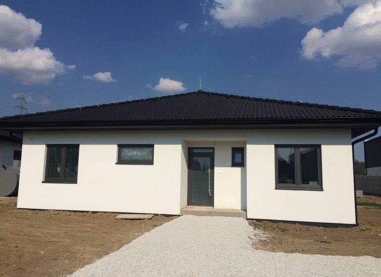 Výstavba moderného 4 izbového murovaného bungalovu - Rodinný dom v Trnave s bielou fasádou a tmavou strechou pod modrou oblohou.