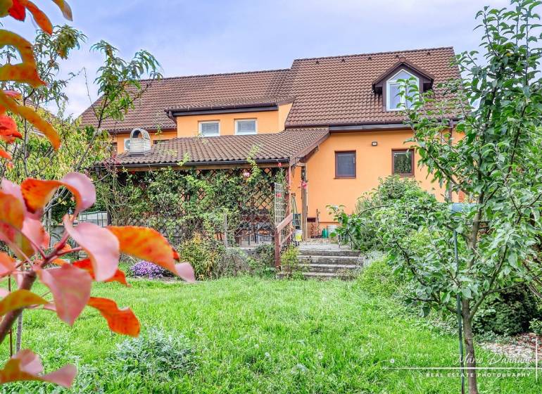 5-izbový rodinný dom s dvomi garážami v obci Špačince - Rodinný dom v Špačinciach na Špačinskej ulici s upravenou záhradou a oranžovou fasádou.