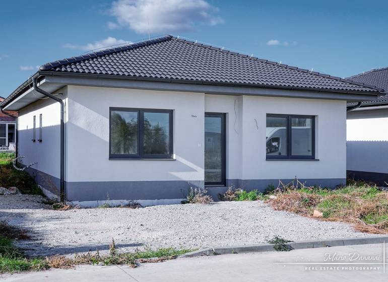 Novostavba 4-izbového rodinného domu v obci Slov.Nová Ves - Rodinný dom v Slovenskej Novej Vsi na ulici Slovenská Nová Ves s tmavou strechou a parkoviskom.