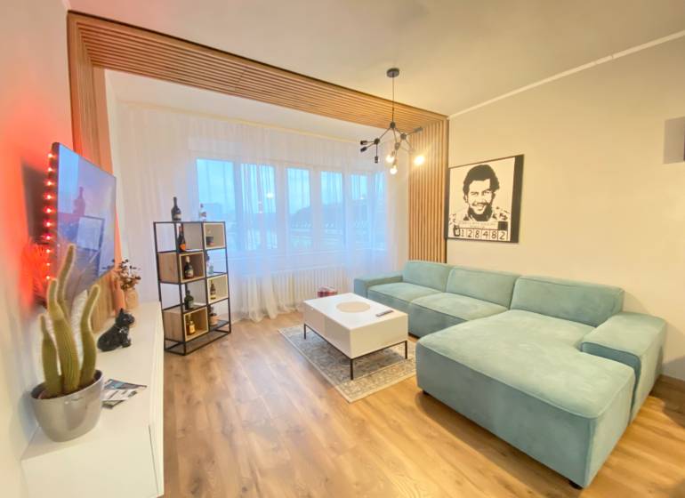 NA PRENÁJOM NADŠTANDARDNÝ 2-IZBOVÝ BYT V CENTRE MESTA - Obývacia izba s tyrkysovou sedačkou, podlahou s dreveným dekorom a moderným osvetlením v 2-izbovom byte.