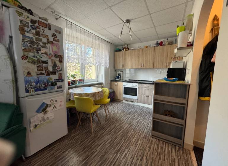 REZERVOVANÉ jednoizbový zrekonštruovaný byt v širšom centre mesta - Kuchyňa s podlahou s dreveným dekorom, jedálenským stolom a chladničkou v 1-izbovom byte.