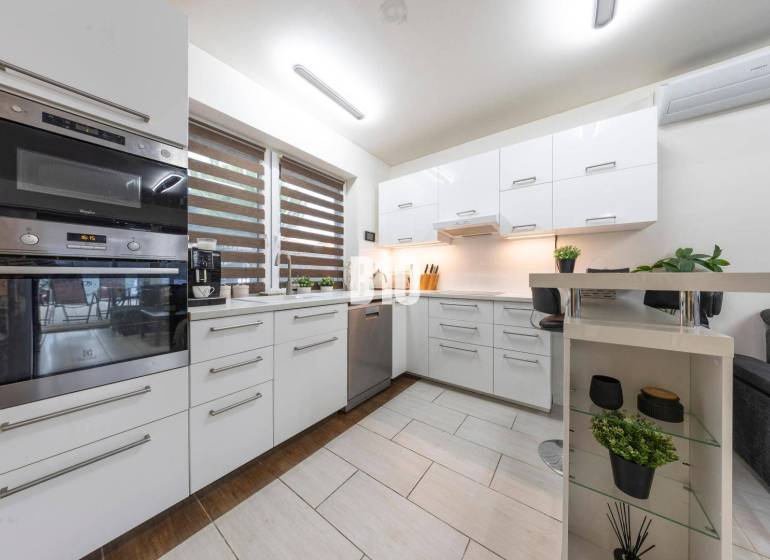 Tri Vody - 4-izbový rodinný dom s bazénom | Most pri Bratislave – Baza - Kuchyňa v rodinnom dome s bielymi skrinkami a oknom so žalúziami.