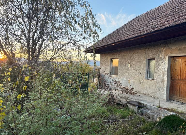 RD TVRDOMESTICE, pozemkom s prístupom z oboch strán - Rodinný dom v Tvrdomesticiach pri západe slnka, v obklopení zelenej vegetácie.