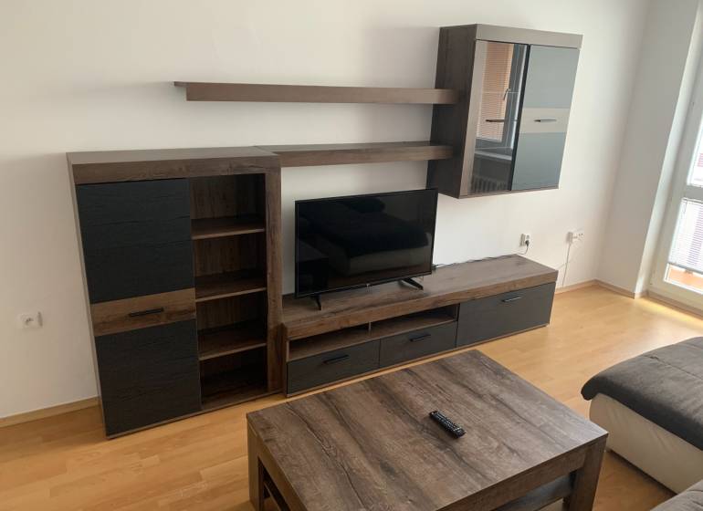 PRIESTRANNÝ 2-IZB BYT,LOGGIA, ATRAKTÍVNA LOKALITA, NOVÉ MESTO - Obývacia izba s tmavým nábytkom a podlahou s dreveným dekorom v 2-izbovom byte.